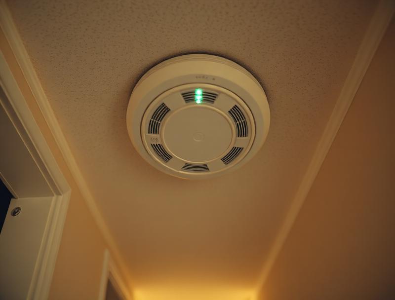 White ceiling-mounted smoke alarm in a residential hallway, green status light illuminated.